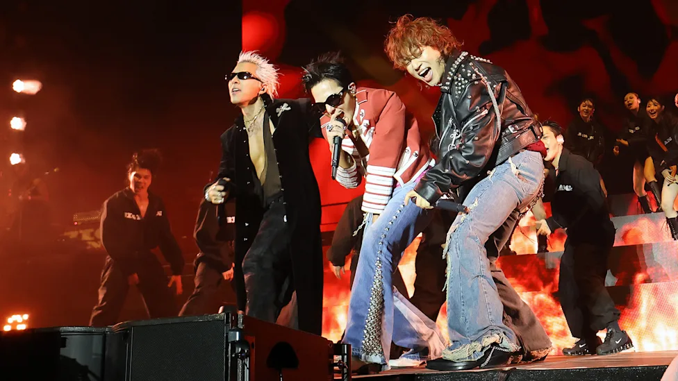 Members of BIGBANG performing together on stage with red pyrotechnics behind them