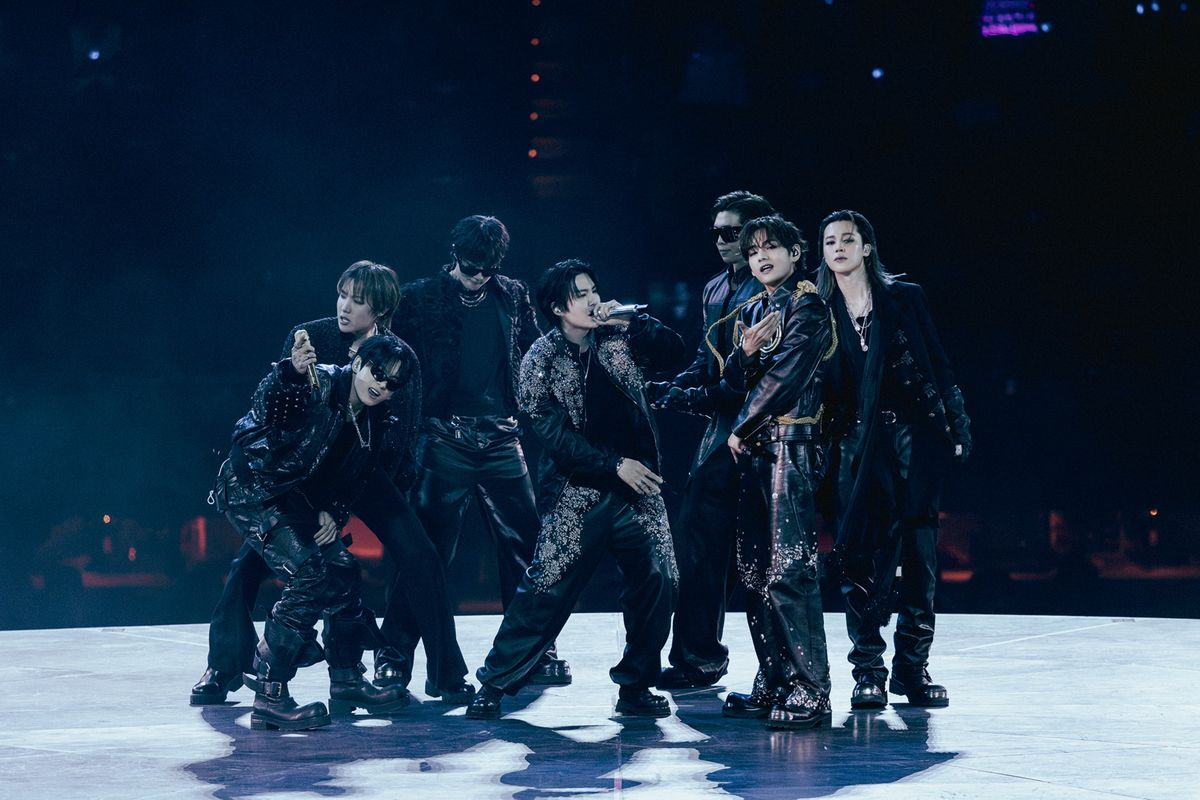 All seven members of BTS performing together on stage in coordinated black outfits