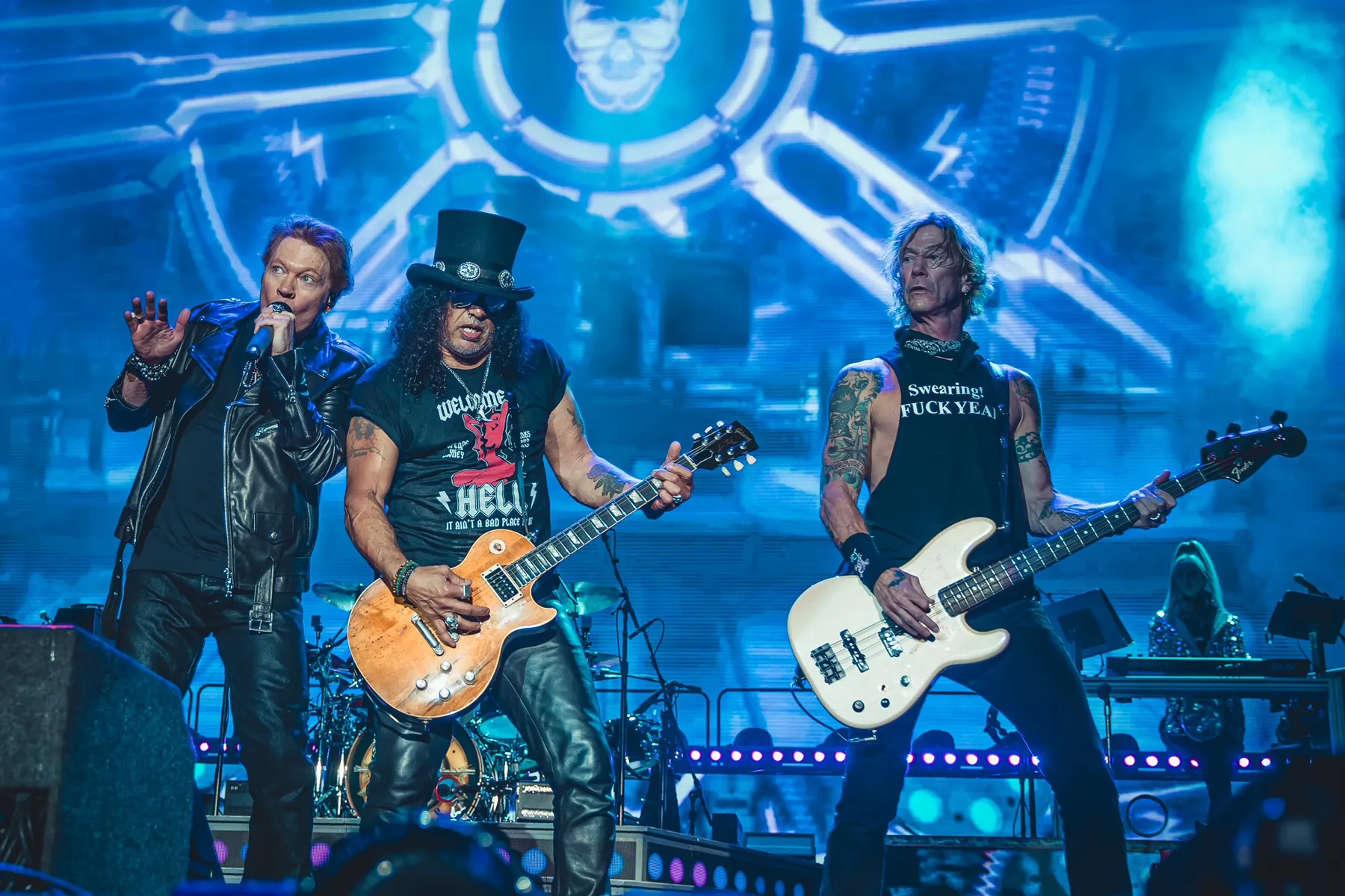 Axl Rose, Slash and Duff McKagan of Guns N' Roses performing on stage under blue lighting
