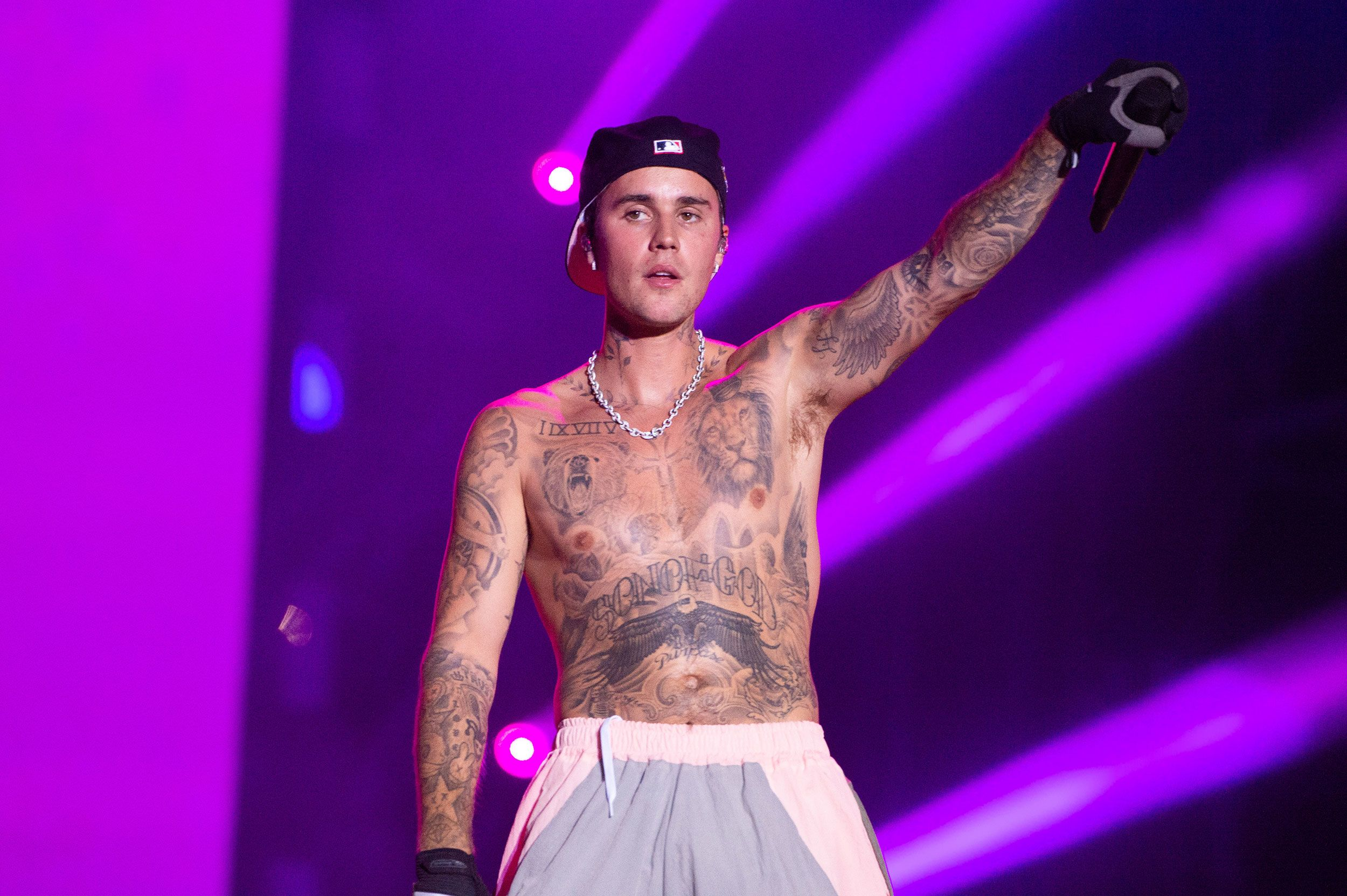 Justin Bieber performing on stage under purple lighting, arm raised