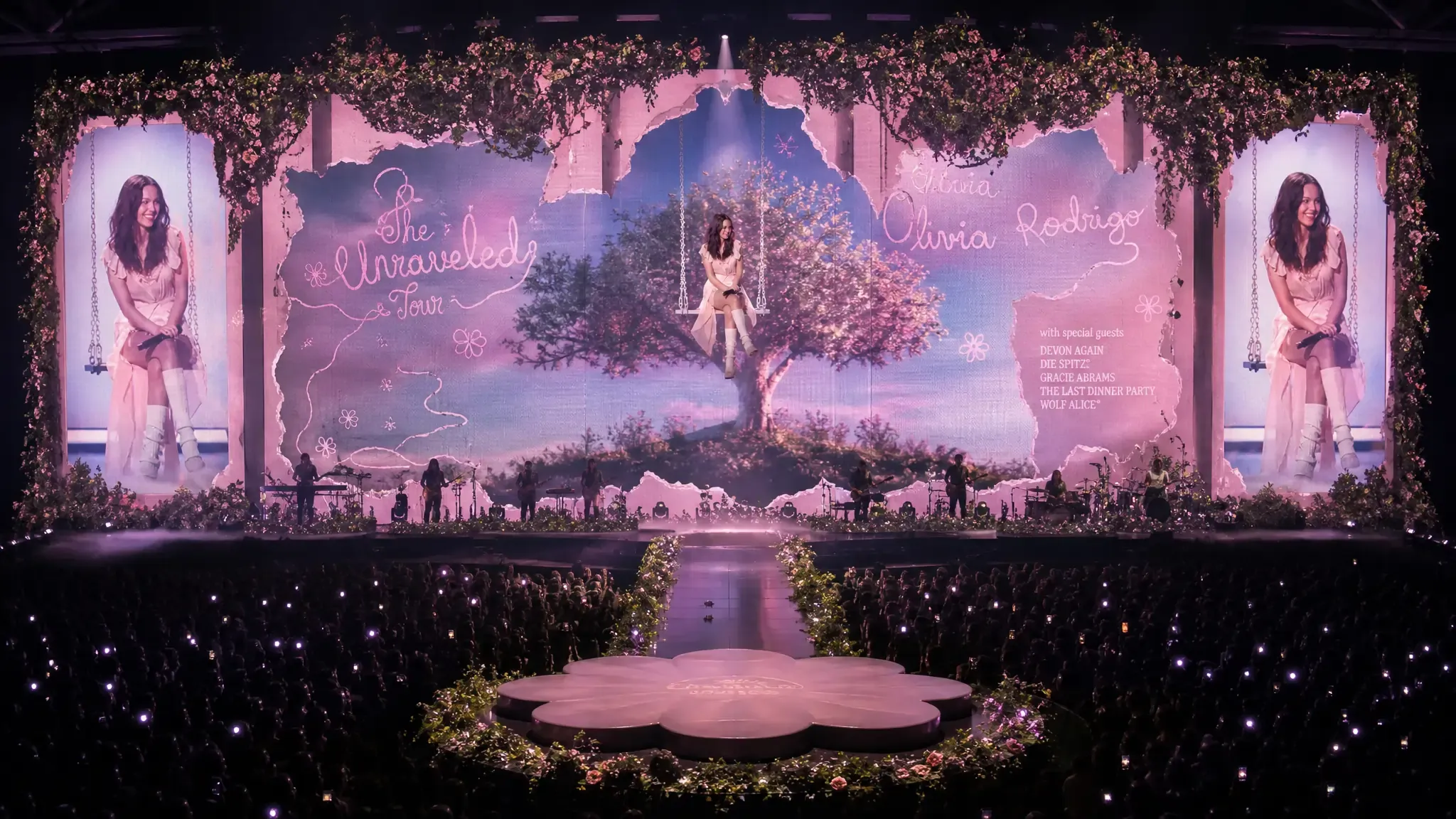 Olivia Rodrigo's Unraveled Tour stage set, with her name and tour title projected on screens flanking a tree centrepiece