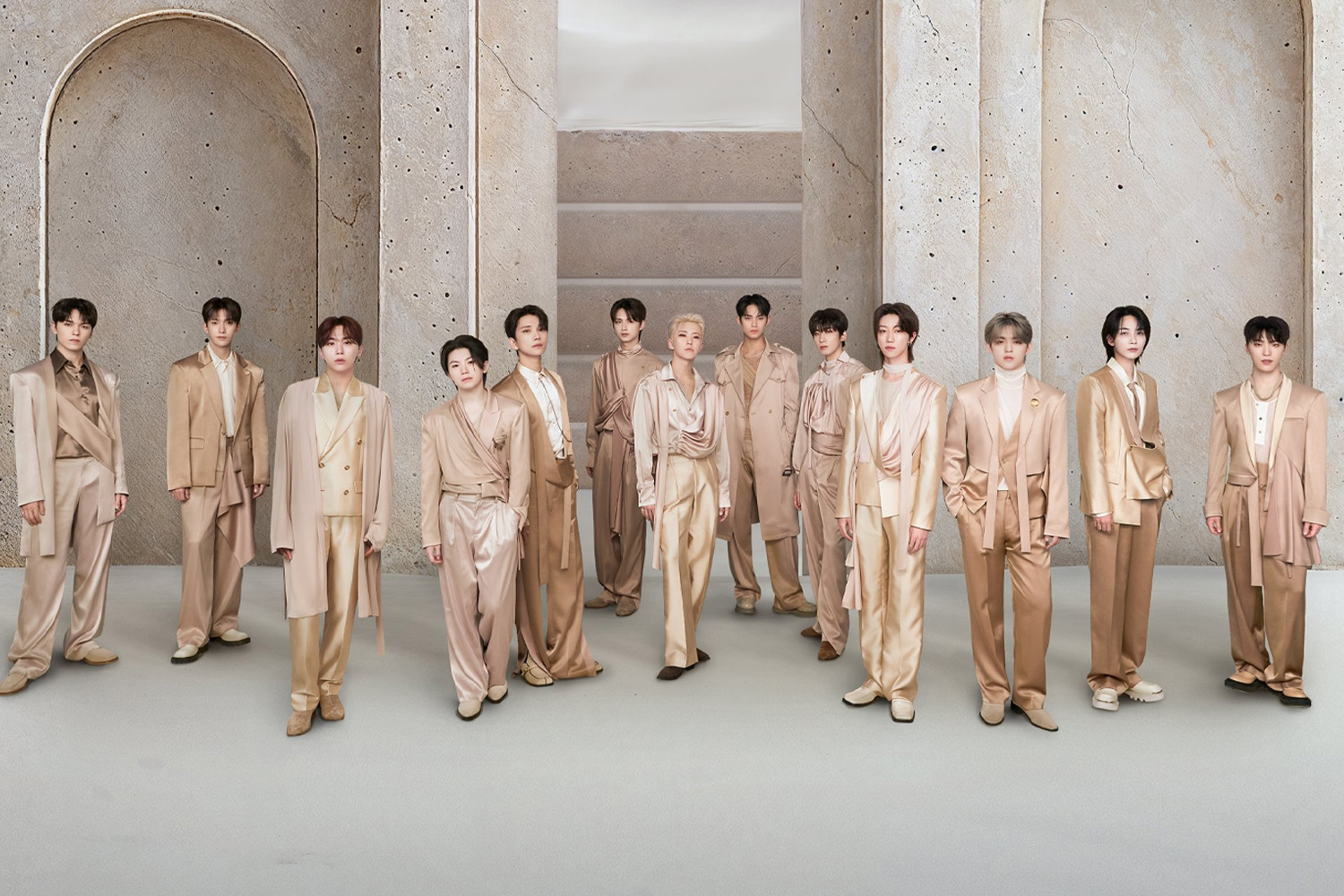 The thirteen members of SEVENTEEN standing together in coordinated beige and cream outfits