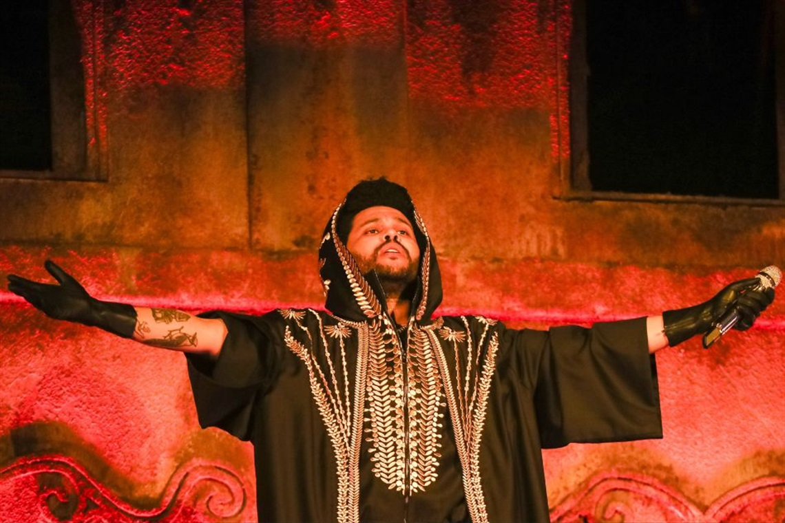 The Weeknd performing on stage in an embroidered black robe with arms outstretched