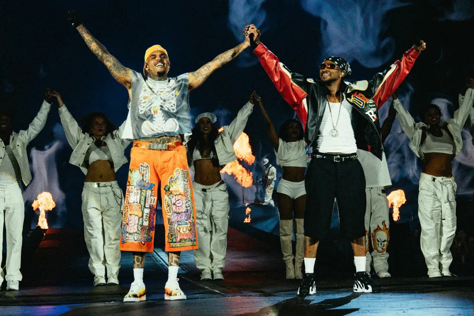 Chris Brown and Usher on stage with arms raised together, surrounded by dancers and pyrotechnics